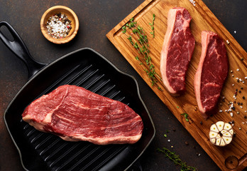 Raw fresh meat Picanha steak, traditional Brazilian cut with thyme, garlic, and black pepper on wooden board. Sliced meat Black Angus steak on grill iron pan. Top view.