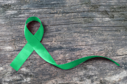 Green ribbon awareness symbolic bow for Kidney, Gallbladder, Bile Duct Cancer, Glaucoma, Leukemia, Traumatic Brain Injury, and Mental Health illness (bow isolated on aged wood with clipping path)