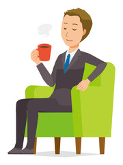 A young businessman is sitting on the sofa and drinking coffee