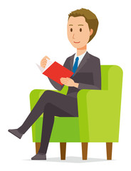 A young businessman is sitting on a sofa and reading books