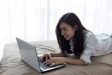 Woman using laptop computer on her bed, In the white bedroom by the window