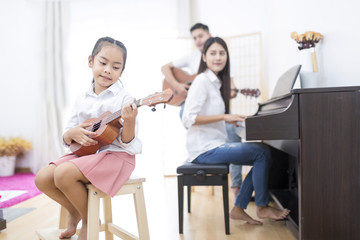 Asian family,daughter playing ukulele,father playing guitar,mother playing piano