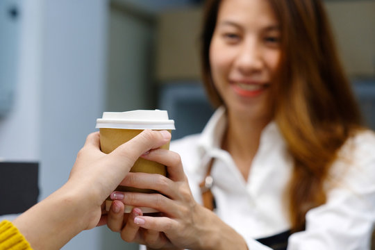 Young asia woman barista serving a diaposable coffee cup with smiling face at cafe counter background, small business owner, food and drink industry concept