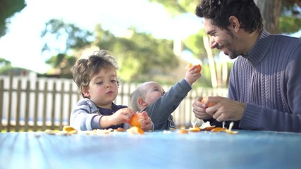 A father with two little sons peeling and eating tangerines in the garden