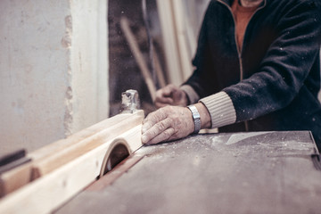 An elderly carpenter saws a wooden workpiece.