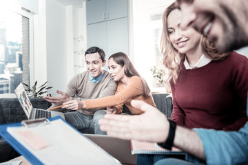 Check it out. Interested perspective pleasant employees working in pairs in the office sitting on the sofa and using the laptop.