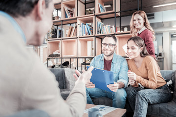 Obraz premium Some advices. Friendly smart nice-looking colleagues sitting in the room on the sofa listening to their friend and looking at him.