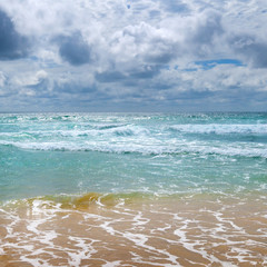 Sandy beach of the tropical ocean and the overcast sky with dramatic clouds.