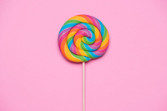 Rainbow lollipop swirl on wooden stick on pink paper background