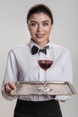 Red wine. Charming optimistic good looking woman smiling and stretching salver where glass of wine standing