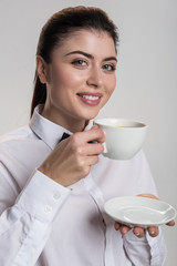 Pleasant drink. Elegant merry jolly woman carrying cup and gazing at the camera  while drinking coffee