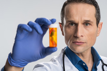 Medical test. Experienced adorable male doctor holding bottle of pills and wearing gloves while standing on the isolated background 