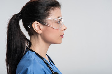 True in future. Thoughtful determined female physician putting on safety glasses while reflecting and staying  in profile