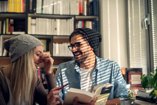 Close up of happy attractive beautiful hardworking stylish hipster young couple laughing while reading a book together in the library or classroom near the sunny window.