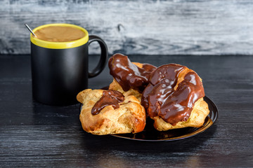 Coffee and chocolate eclairs on a dark wooden background