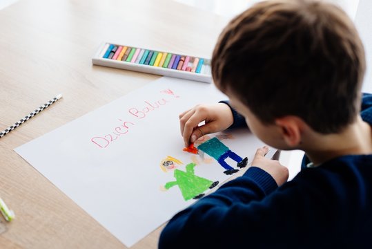 8 letni chłopiec maluje kredkami obrazek lurkę dla swojej babci na Dzień Babci