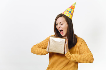 Cheerful caucasian crazy young happy woman in yellow clothes, birthday party hat holding golden gift box with present, celebrating and enjoying holiday on white background isolated for advertisement.