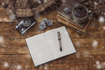 Diary with pen, books, aluminum vintage cup with hot tea, antique photo camera and Christmas bumps on a wooden background. Added snowfall effect