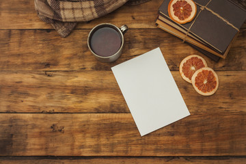 A sheet of paper, books, an aluminum antique cup with coffee and a blanket on a wooden table