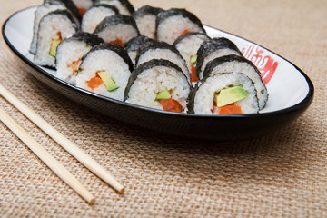 Sushi rolls in nori seaweed with avocado and red fish on ceramic plate and wooden sticks