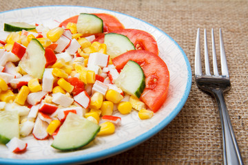 Salad with crab sticks, boiled corn and freshly sliced tomato and cucumber on plate with fork