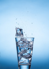 Splashing water drinking glass with ice cubes on blue background