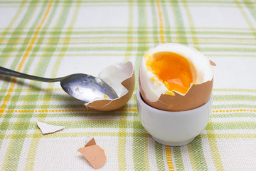 Boiled fresh smash broken egg for the breakfast on the porcelain stand for eggs. Broken beige hen egg and pieces of shells, bright liquid orange yolk in the spoon.