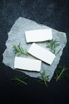 Sliced feta cheese with rosemary on rustic paper.