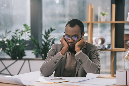 thoughtful african american architect looking at blueprints in office