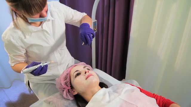 The woman on the procedure of lightening the skin. The beautician treats the nose of a girl lying on the couch.