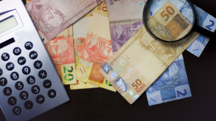 Notas de dinheiro acompanhado de moedas, carteira de trabalho, lupa, calculadora encima da mesa