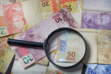 Notas de dinheiro acompanhado de moedas, carteira de trabalho, lupa, calculadora encima da mesa