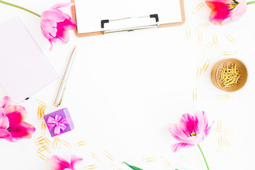 Home workspace with clipboard, diary, pink flowers and accessories on white background. Flat lay, top view. Blogger or freelancer composition.