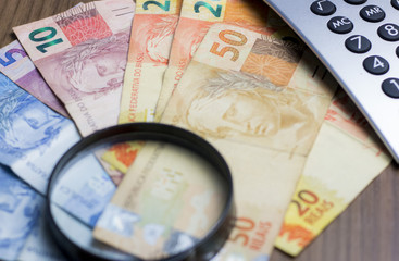 Notas de dinheiro acompanhado de moedas, carteira de trabalho, lupa, calculadora encima da mesa