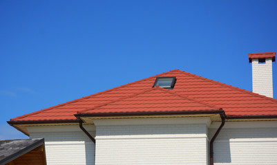 Fototapeta na wymiar House with metal roof tiles, attic skylight windows. Home Guttering, roof gutters, plastic guttering system.