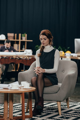 young beautiful businesswoman sitting on armchair and looking at papers on table