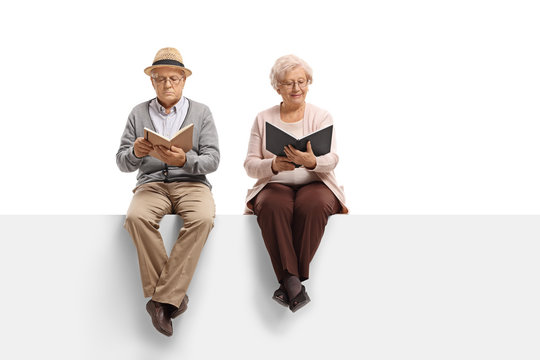 Mature man and an elderly woman sitting on a panel and reading books