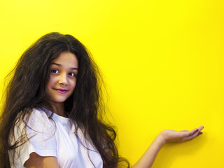 Young woman pointing to empty copy space, isolated on yellow.