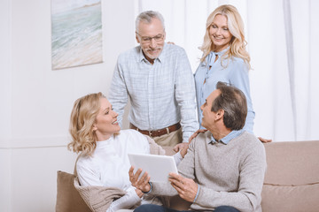 Senior men and women using digital tablet while sitting on sofa