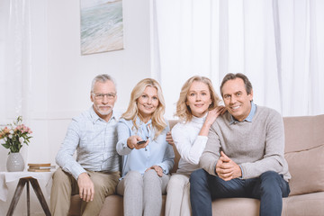 Senior men and women sitting on sofa and watching tv using remote control