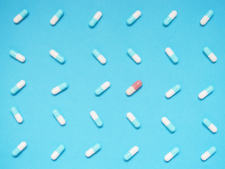 Unique brown capsule among many blue and white capsule on blue background. Creative idea for uniqueness, innovation, different thinking, individuality, contrast and pharmaceutical concept.