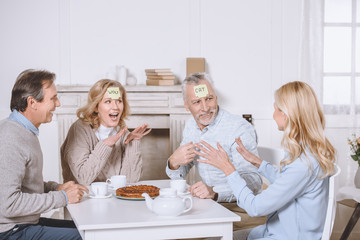 friends playing card game with words on foreheads while sitting at table