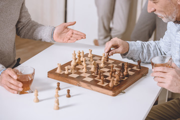 cropped image of men playing chess while sitting at table