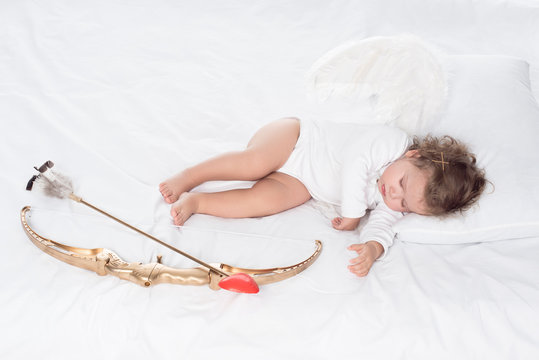 little angel with wings lying on bed with bow and arrow