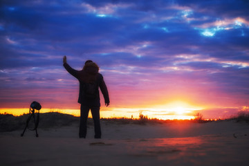 Fototapeta premium The photographer shoots landscapes during the sunset on the sand. Beautiful colorful sunrise sky. Creativity and success.