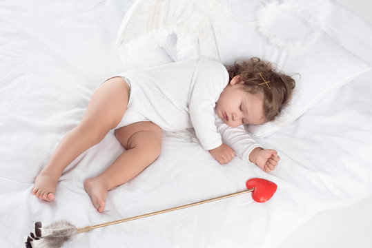 little cupid with wings sleeping on bed with arrow