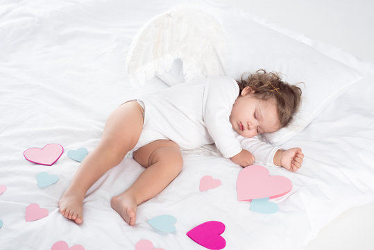 little cherub with wings sleeping on bed with hearts