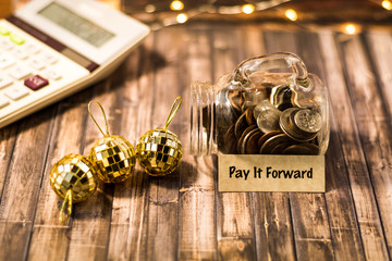 Pay It Forward money jar savings concept on wooden board 