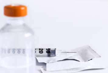Injection vial, syringe and alcohol pad for disinfection on a white table.
