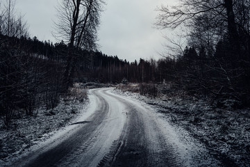 Obraz premium Dunkle Forststraße mit etwas Schnee führt durch den Wald